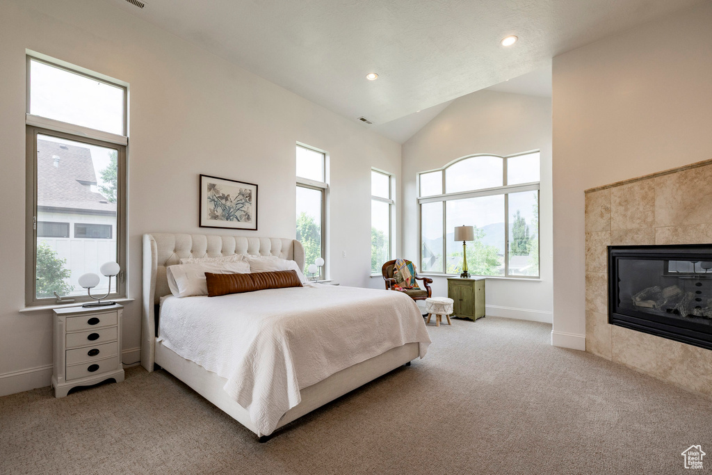 Bedroom with light colored carpet, baseboards, a tiled fireplace, high vaulted ceiling, and recessed lighting