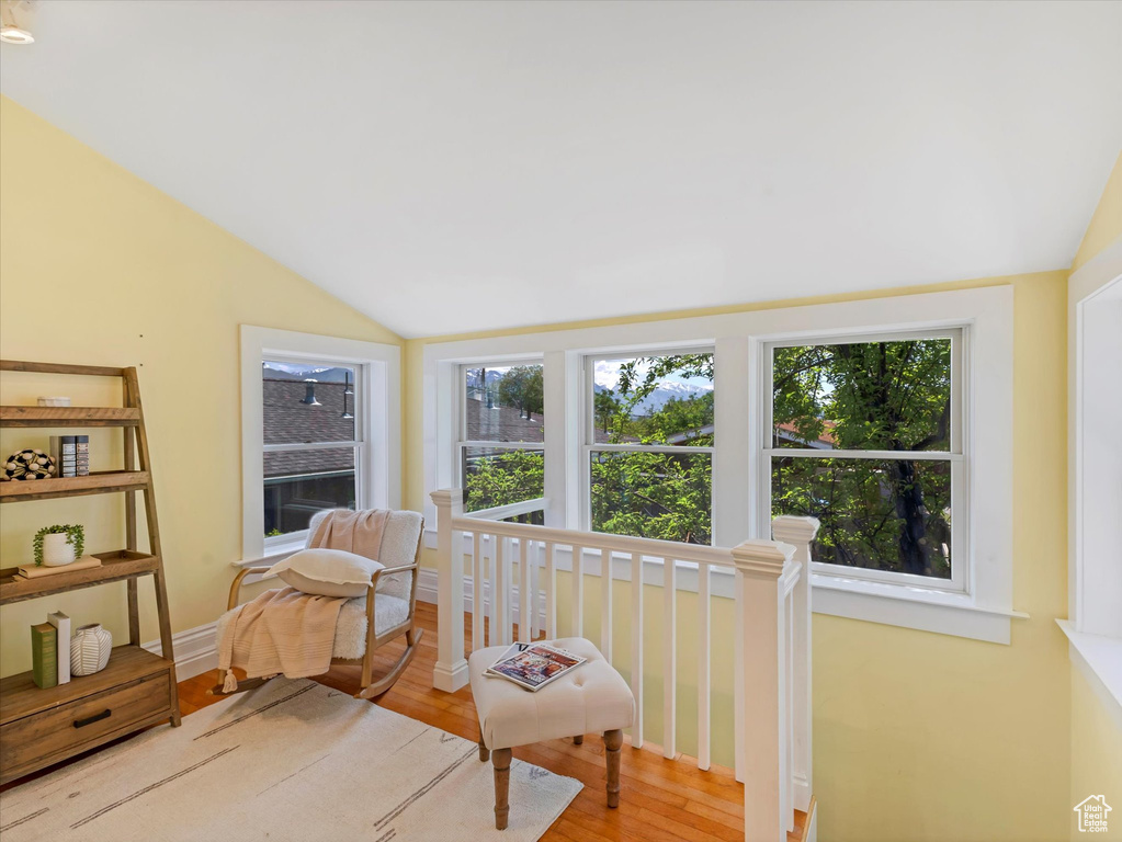 Living area with lofted ceiling, plenty of natural light, wood finished floors, and an upstairs landing