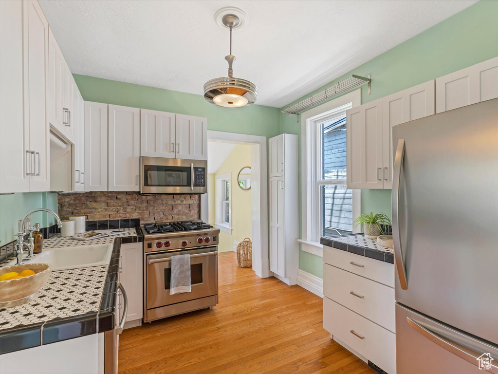 Kitchen featuring appliances with stainless steel finishes, a sink, white cabinetry, backsplash, and light wood-style flooring