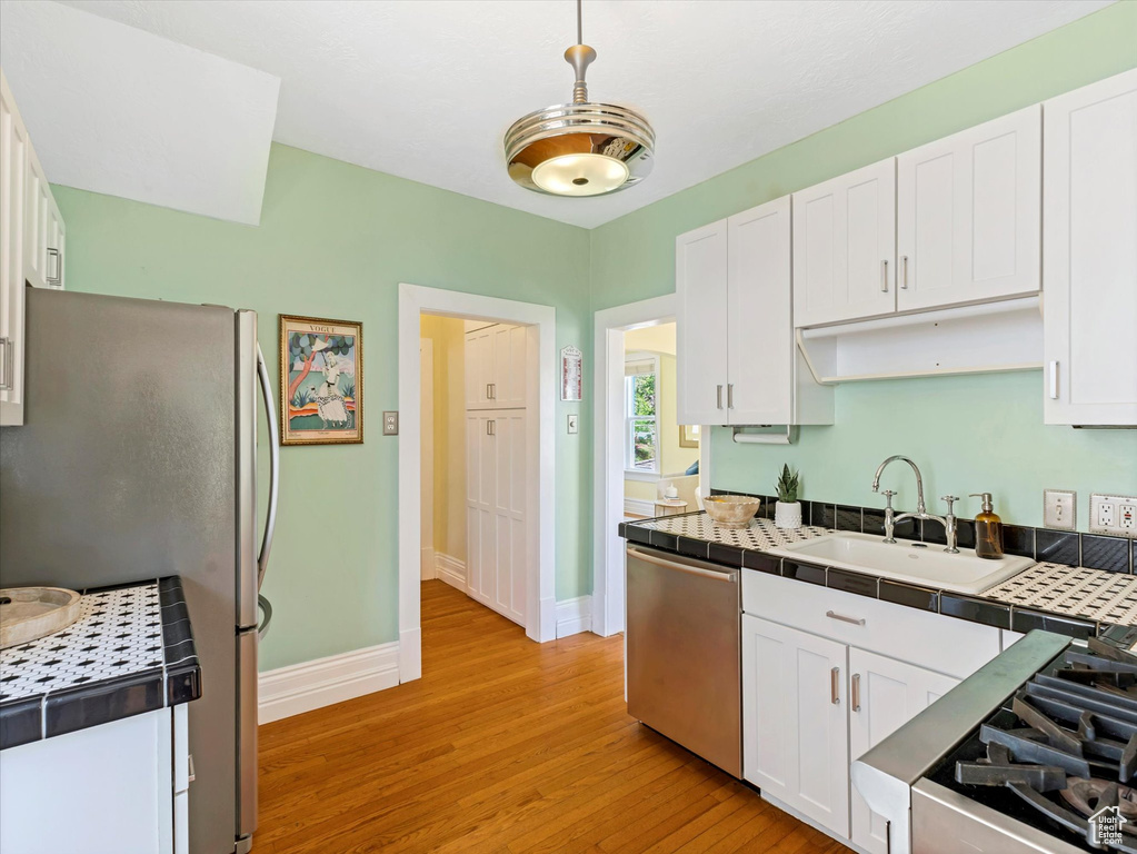 Kitchen with stainless steel appliances, a sink, tile countertops, baseboards, and white cabinets