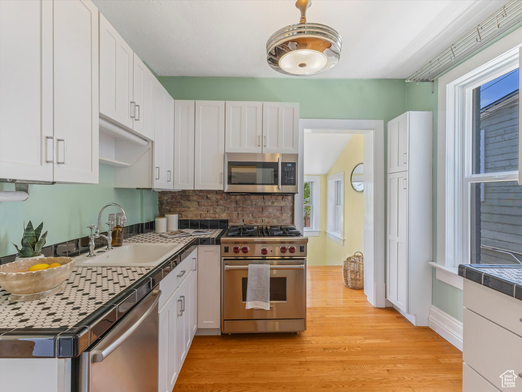 Kitchen with stainless steel appliances, a sink, white cabinets, light wood-style floors, and tasteful backsplash