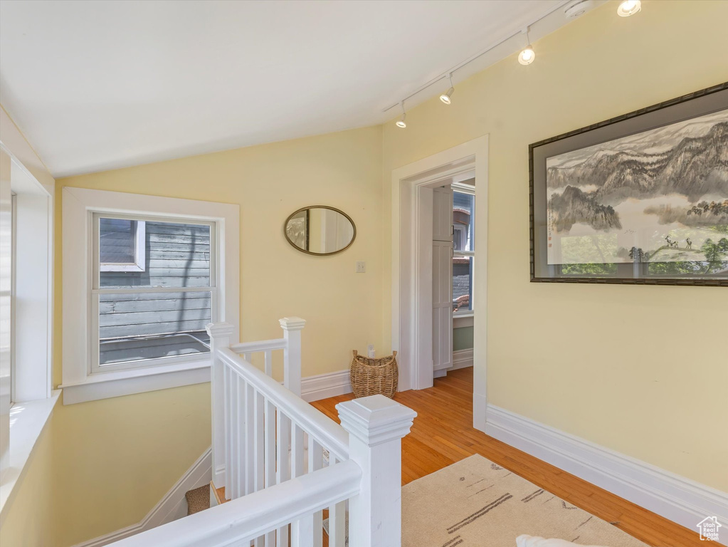 Hall with an upstairs landing, wood finished floors, rail lighting, vaulted ceiling, and baseboards