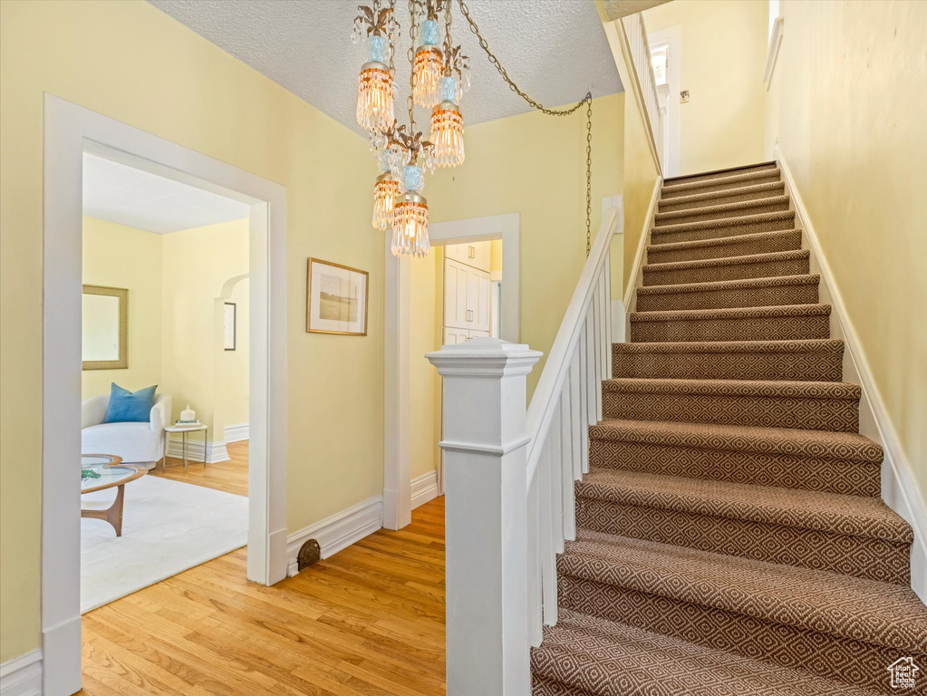 Staircase featuring a chandelier, wood finished floors, baseboards, and a textured ceiling