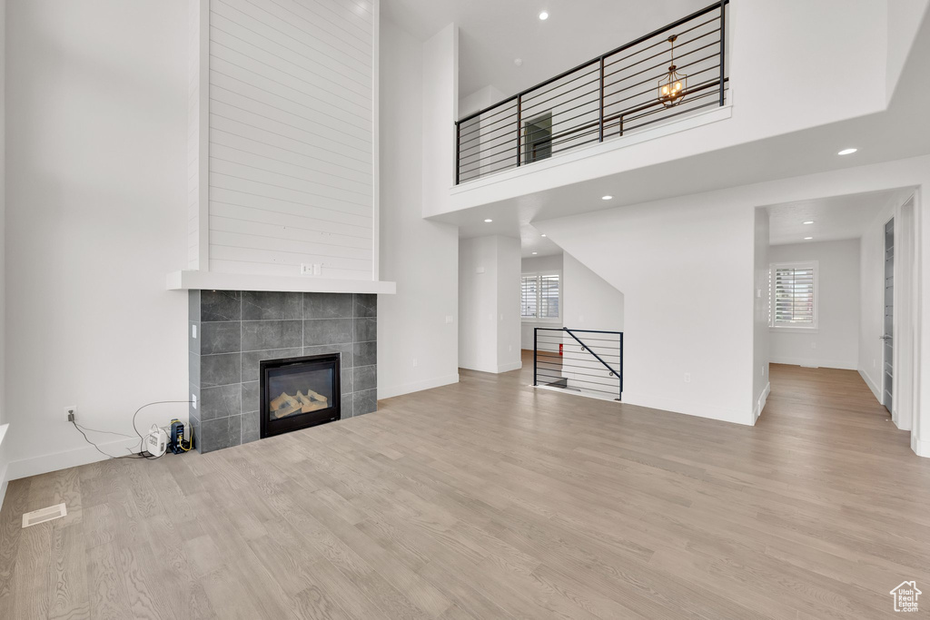 Unfurnished living room featuring plenty of natural light, wood finished floors, a tiled fireplace, recessed lighting, and baseboards