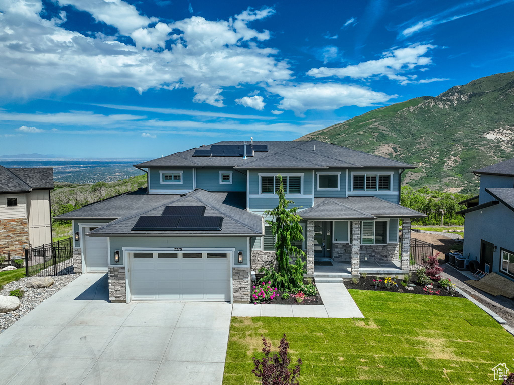 View of front facade featuring solar panels, an attached garage, driveway, and stone siding
