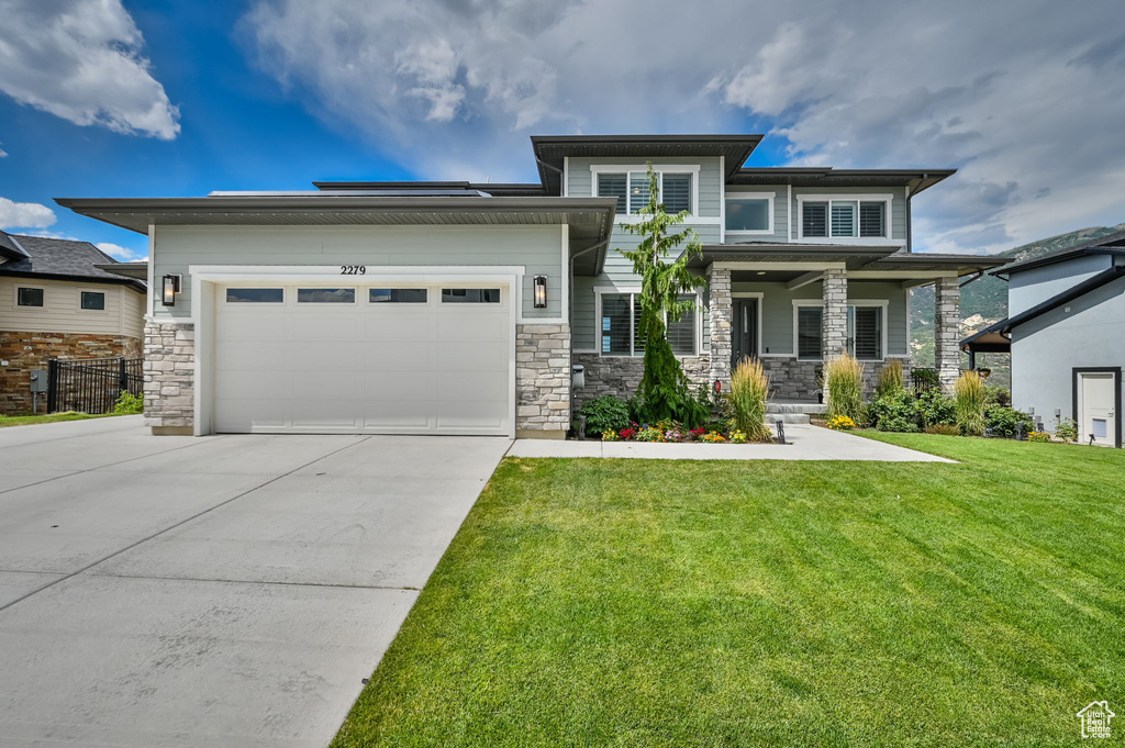 Prairie-style home featuring driveway, a front lawn, a garage, and stone siding
