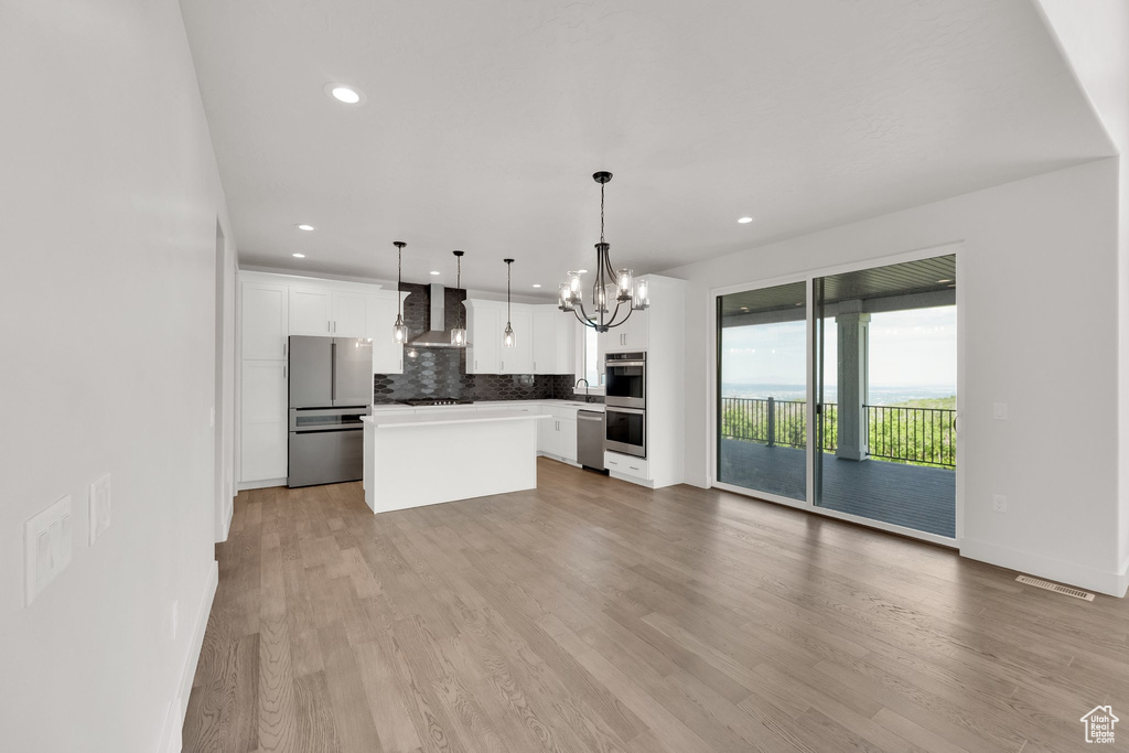 Kitchen featuring stainless steel appliances, wall chimney range hood, a chandelier, backsplash, and white cabinets