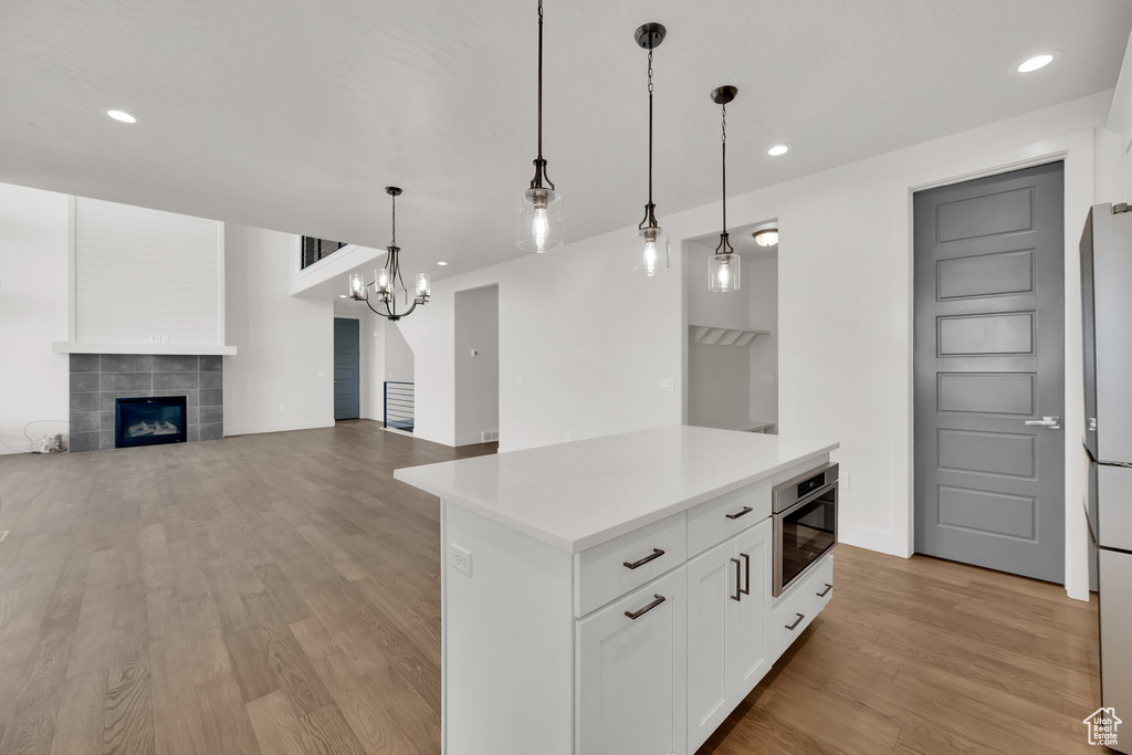 Kitchen featuring light wood finished floors, a tile fireplace, light countertops, white cabinets, and recessed lighting