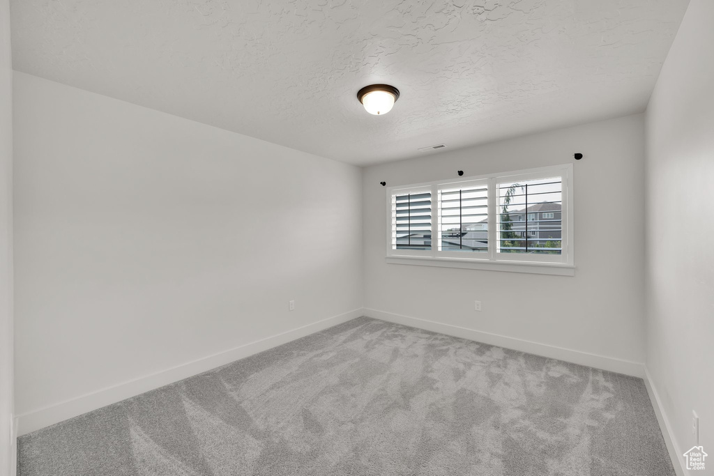Carpeted empty room featuring a textured ceiling and baseboards