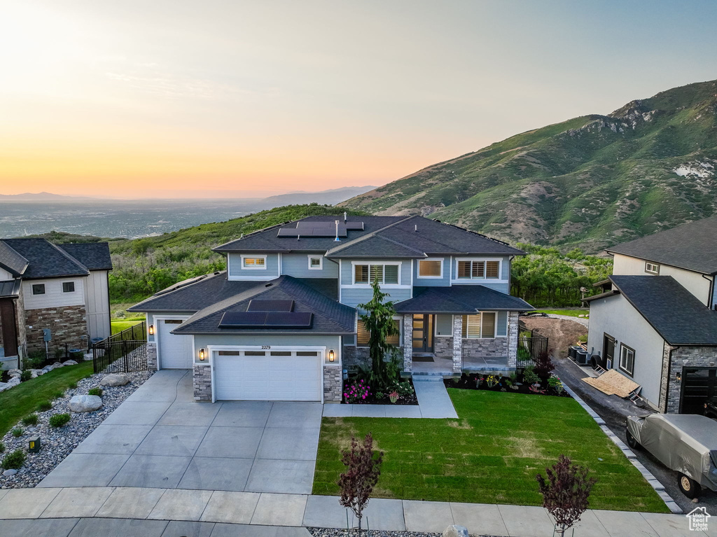 View of front of home with solar panels, driveway, stone siding, a garage, and a mountain view