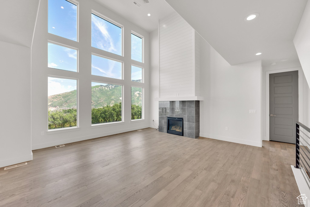 Unfurnished living room featuring a tile fireplace, healthy amount of natural light, a towering ceiling, light wood-style flooring, and recessed lighting