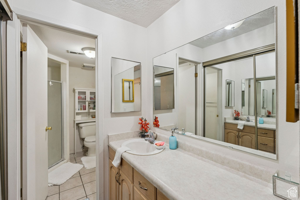 Bathroom with a stall shower, toilet, vanity, tile patterned floors, and a textured ceiling