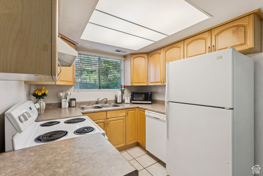 Kitchen featuring white appliances, a sink, light brown cabinetry, range hood, and light tile patterned flooring