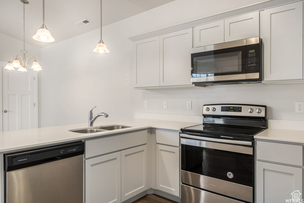 Kitchen featuring stainless steel appliances, a sink, a peninsula, light countertops, and a chandelier