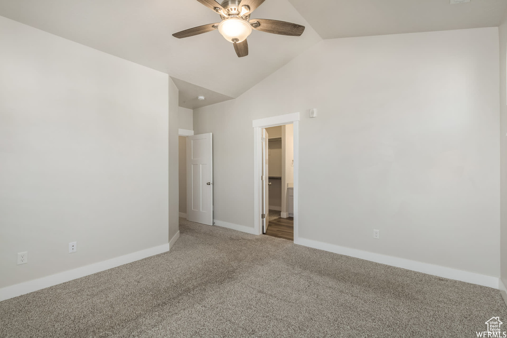 Carpeted spare room with a ceiling fan, vaulted ceiling, and baseboards