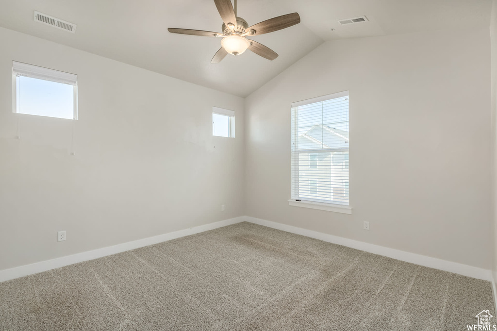 Carpeted empty room with ceiling fan, baseboards, and vaulted ceiling