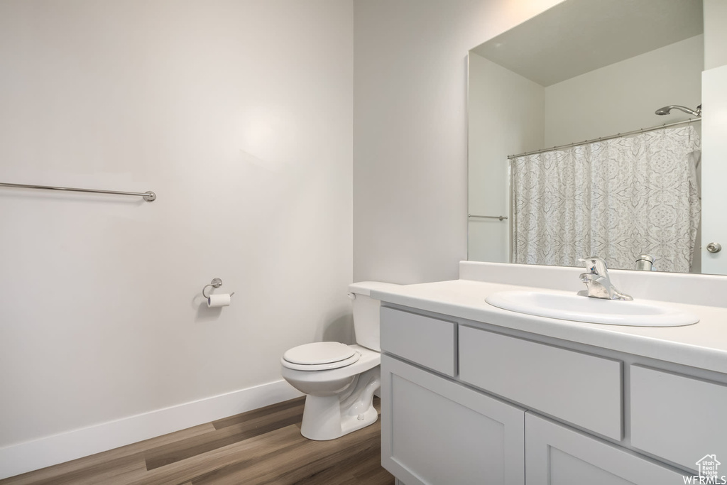 Full bathroom featuring vanity, baseboards, wood finished floors, and toilet