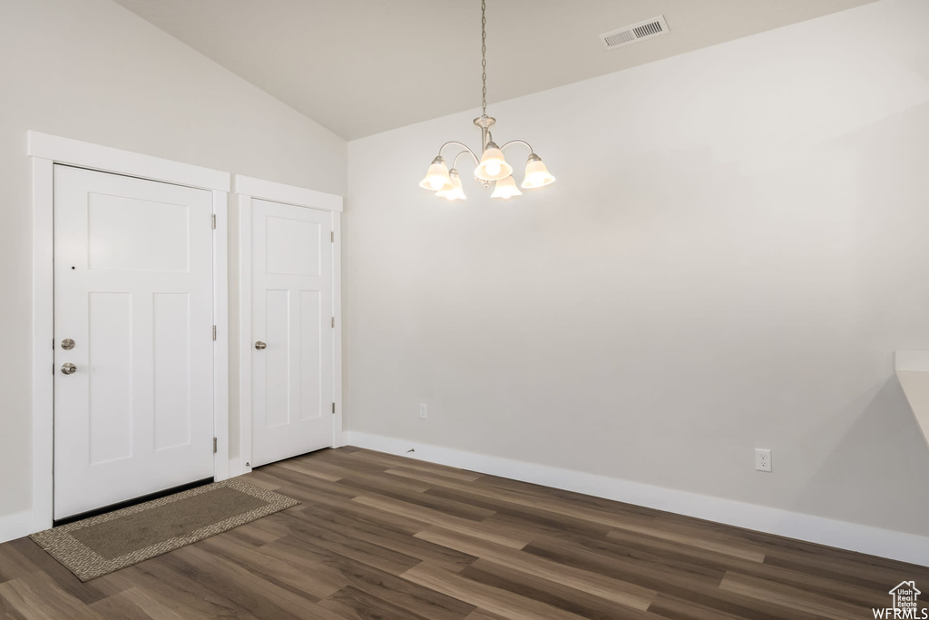 Unfurnished dining area with vaulted ceiling, dark wood-style flooring, a chandelier, and baseboards