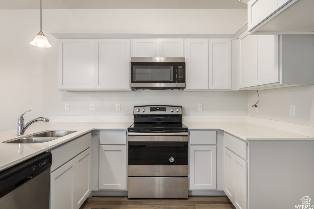 Kitchen with stainless steel appliances, a sink, light countertops, and pendant lighting