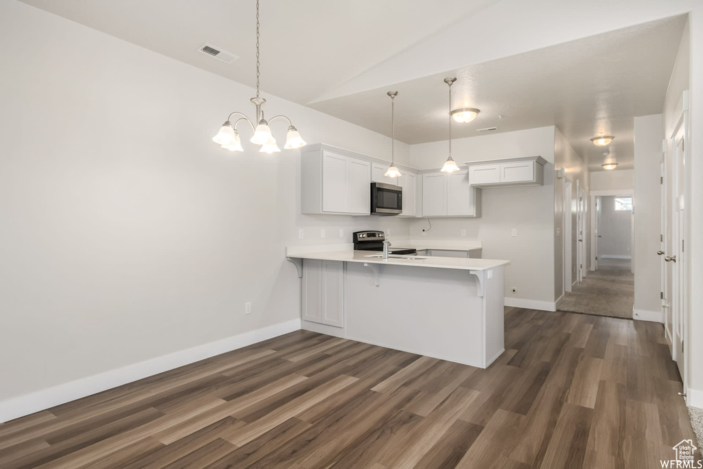 Kitchen with stainless steel appliances, a peninsula, dark wood-style flooring, light countertops, and baseboards