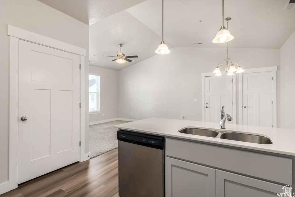 Kitchen featuring stainless steel dishwasher, a sink, wood finished floors, lofted ceiling, and light countertops