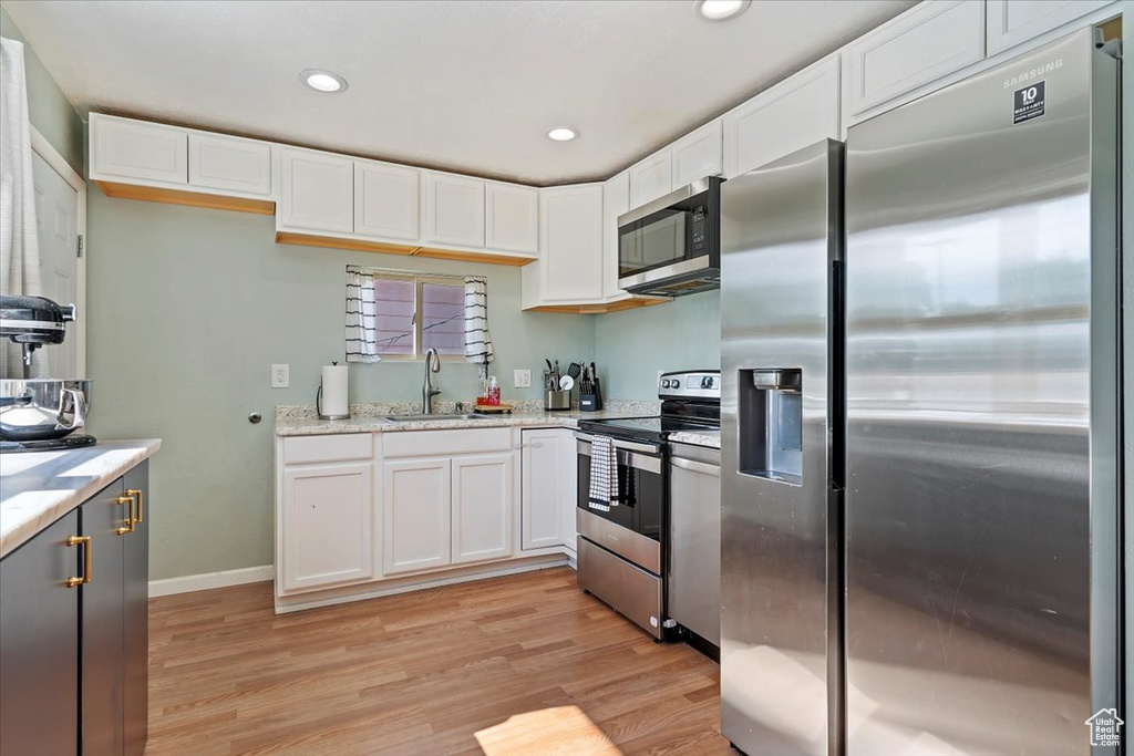 Kitchen with stainless steel appliances, a sink, light wood finished floors, white cabinets, and recessed lighting
