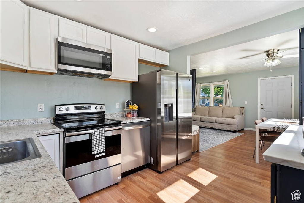 Kitchen featuring appliances with stainless steel finishes, white cabinets, light wood-style floors, open floor plan, and a ceiling fan