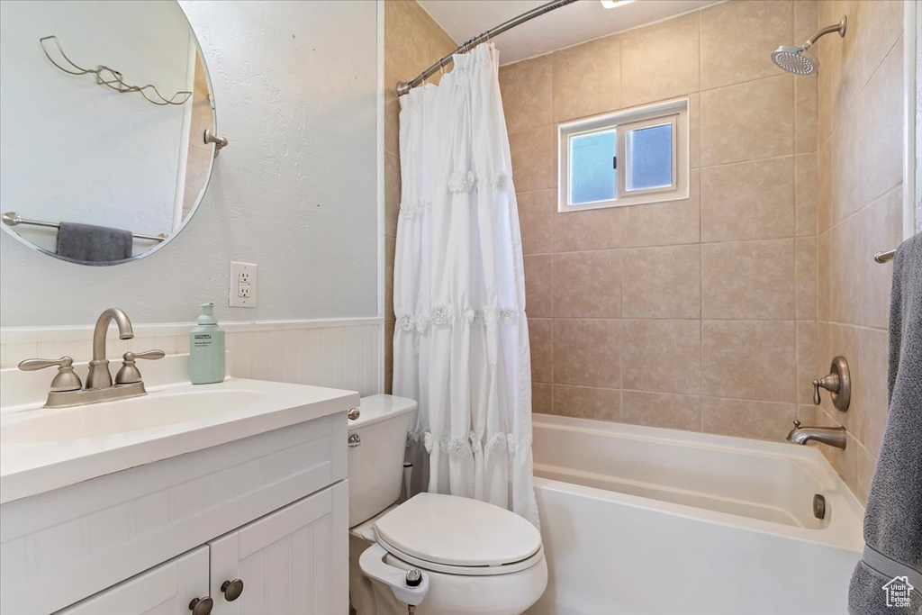 Bathroom with shower / bath combo with shower curtain, toilet, vanity, and a wainscoted wall
