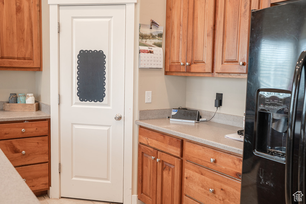 Kitchen with black refrigerator with ice dispenser, light countertops, and brown cabinets