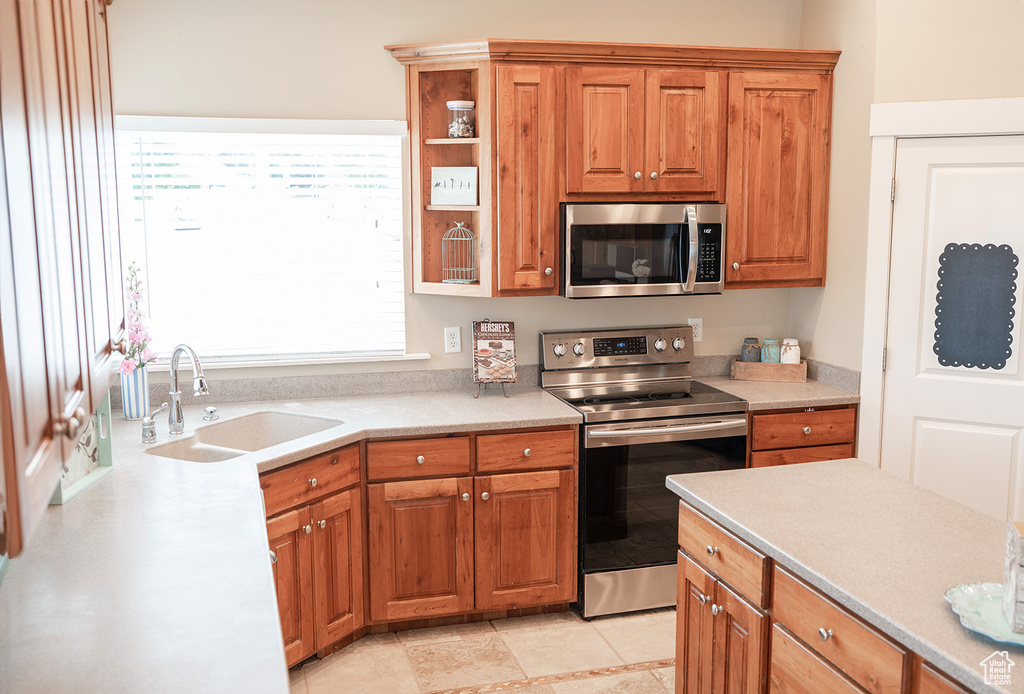 Kitchen with stainless steel appliances, a sink, light countertops, and brown cabinets