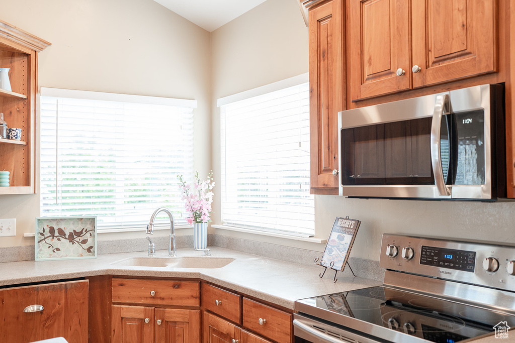 Kitchen with stainless steel appliances, a sink, brown cabinetry, and light countertops
