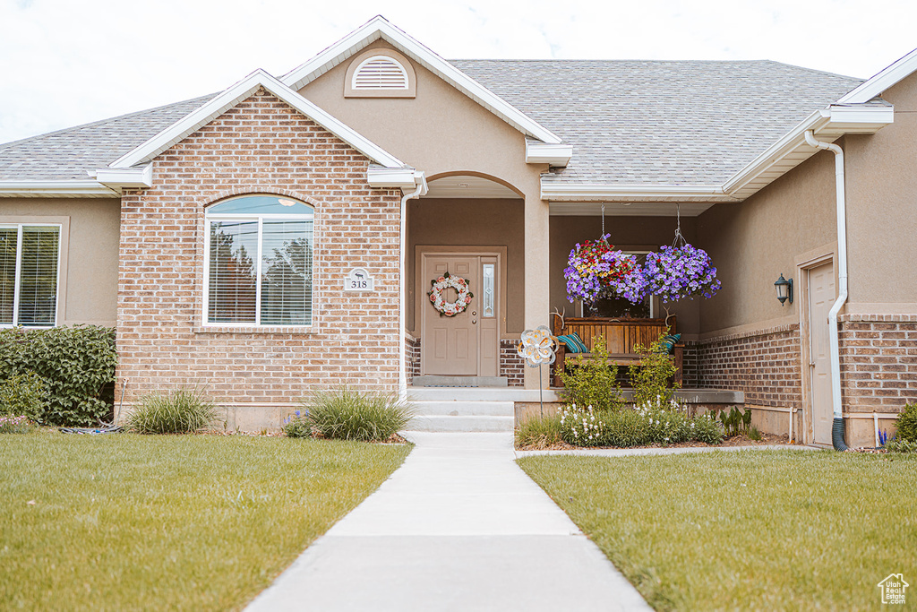 Entrance to property featuring brick siding, a yard, and a shingled roof