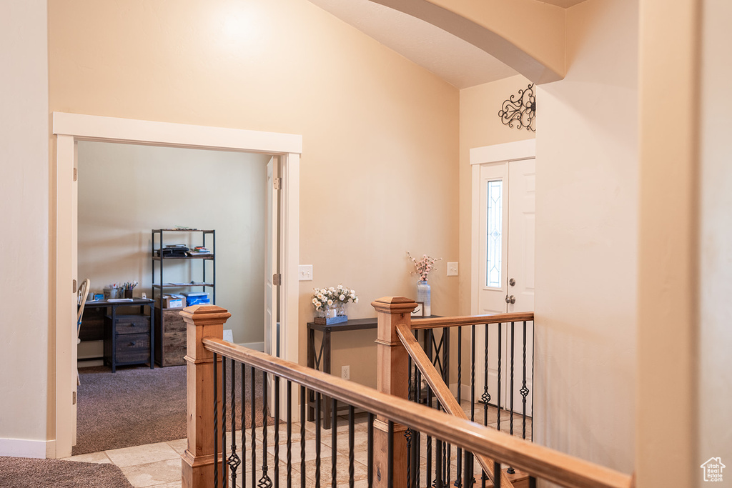 Hallway with an upstairs landing, arched walkways, carpet floors, tile patterned floors, and high vaulted ceiling