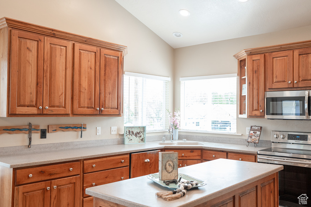 Kitchen with appliances with stainless steel finishes, a sink, brown cabinets, vaulted ceiling, and recessed lighting