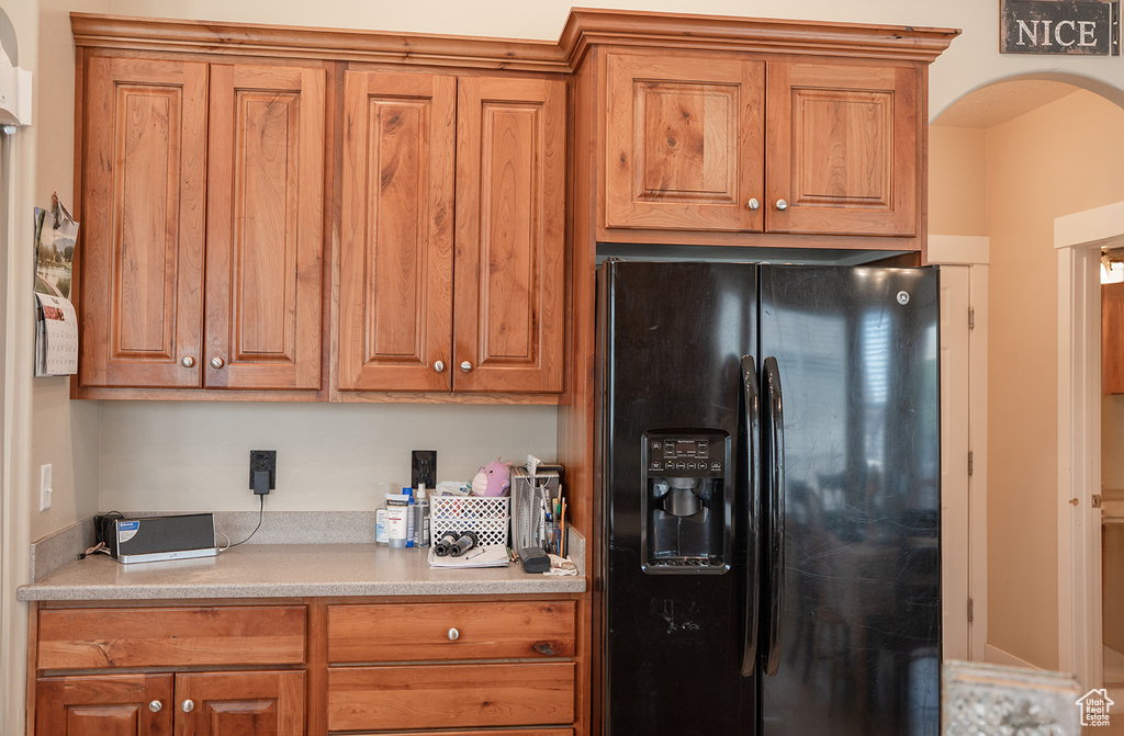 Kitchen with black fridge with ice dispenser, arched walkways, brown cabinets, and light countertops