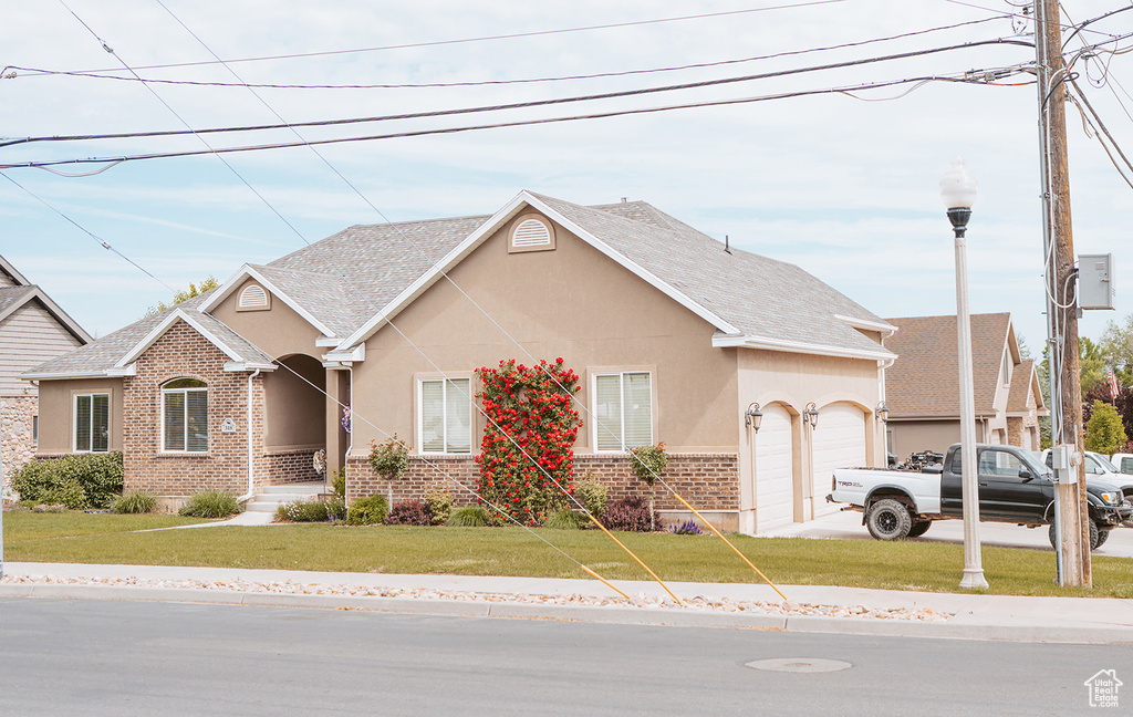 View of front of home featuring brick siding, a garage, stucco siding, a front lawn, and a shingled roof