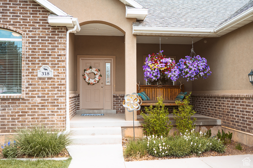 Property entrance with covered porch, brick siding, roof with shingles, and stucco siding