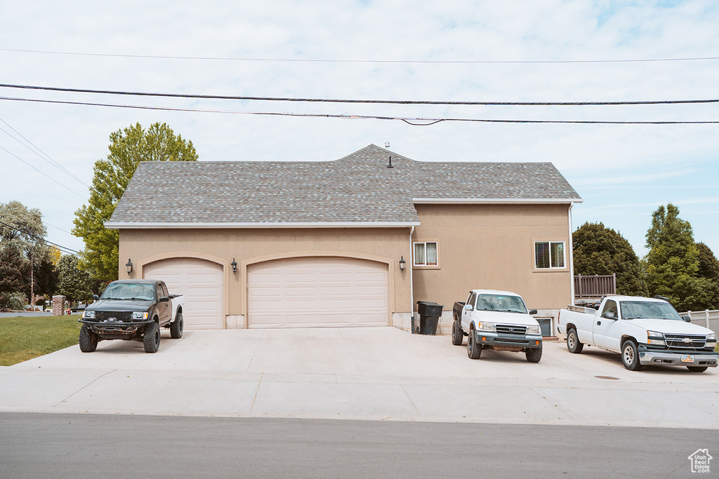 View of side of property with stucco siding, a shingled roof, driveway, and an attached garage