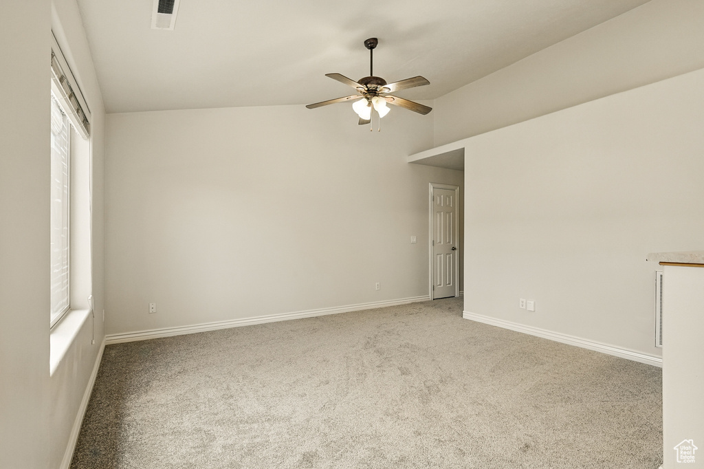 Carpeted empty room with a ceiling fan, lofted ceiling, and baseboards