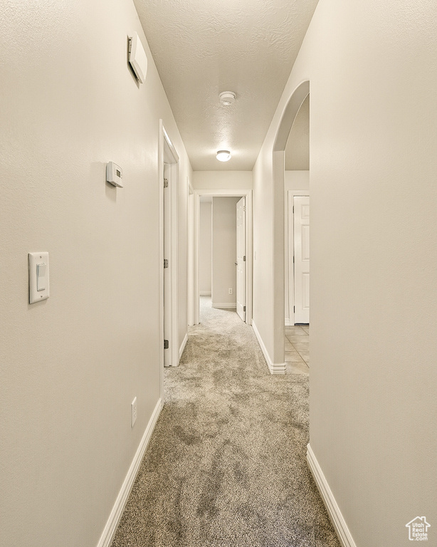 Corridor featuring light carpet, a textured ceiling, baseboards, and arched walkways