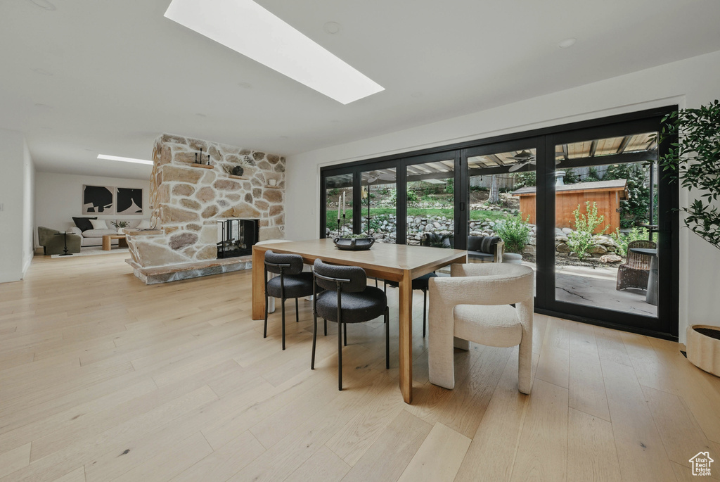 Dining area featuring a stone fireplace, a skylight, and light wood-style flooring
