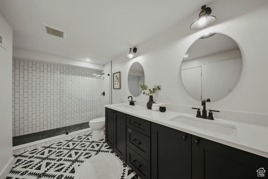 Full bath featuring toilet, double vanity, tiled shower, and tile patterned floors
