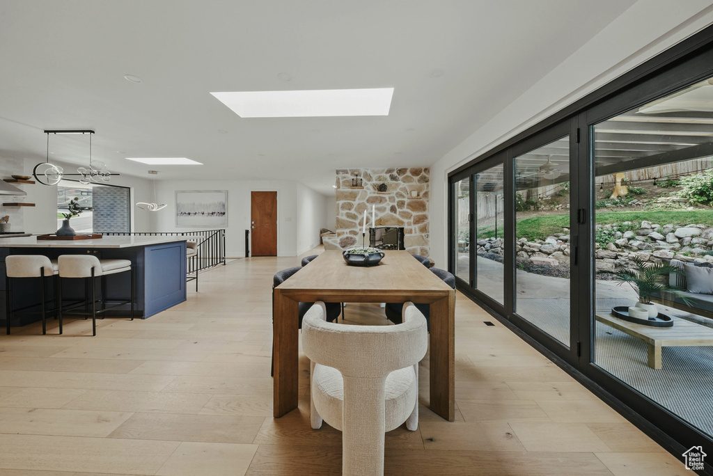Dining room featuring a skylight, healthy amount of natural light, a stone fireplace, and light wood-style floors