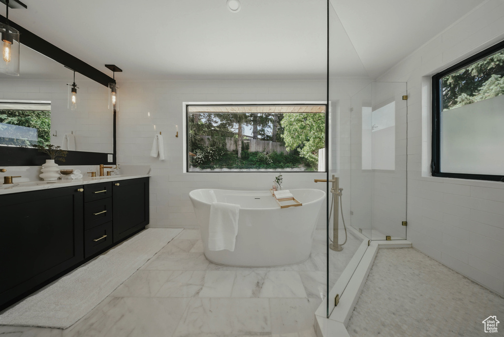 Full bath with plenty of natural light, double vanity, a freestanding tub, tile walls, and marble look tile flooring