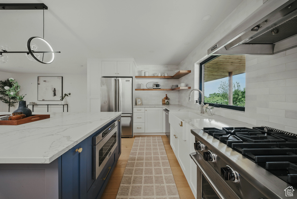 Kitchen with appliances with stainless steel finishes, wall chimney range hood, open shelves, a sink, and white cabinetry