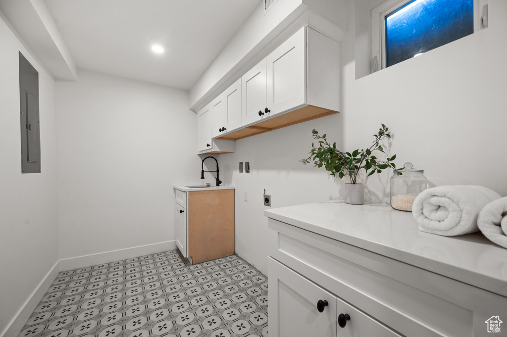Washroom with light flooring, cabinet space, hookup for an electric dryer, electric panel, and baseboards
