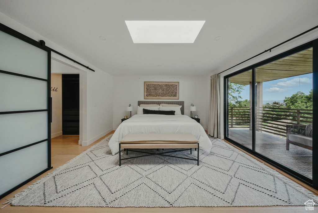 Bedroom featuring access to outside, a skylight, a barn door, light wood-style floors, and baseboards