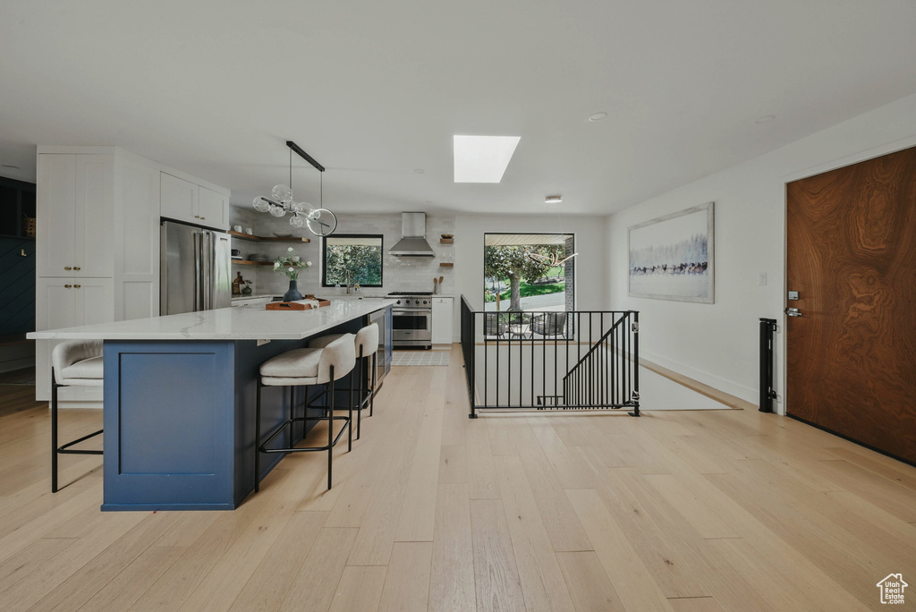 Kitchen featuring appliances with stainless steel finishes, open shelves, wall chimney range hood, a skylight, and white cabinetry