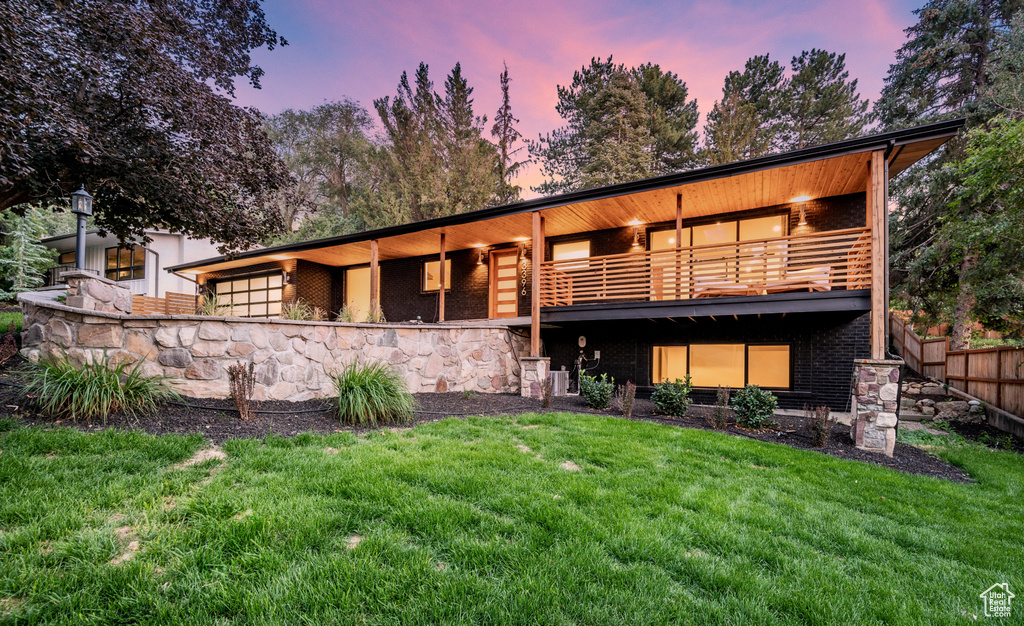 Back of property at dusk featuring a balcony and brick siding