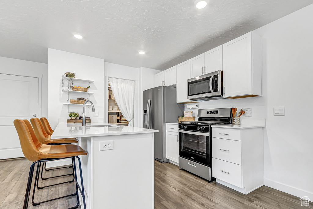 Kitchen with appliances with stainless steel finishes, a sink, light wood-style floors, a breakfast bar area, and light countertops